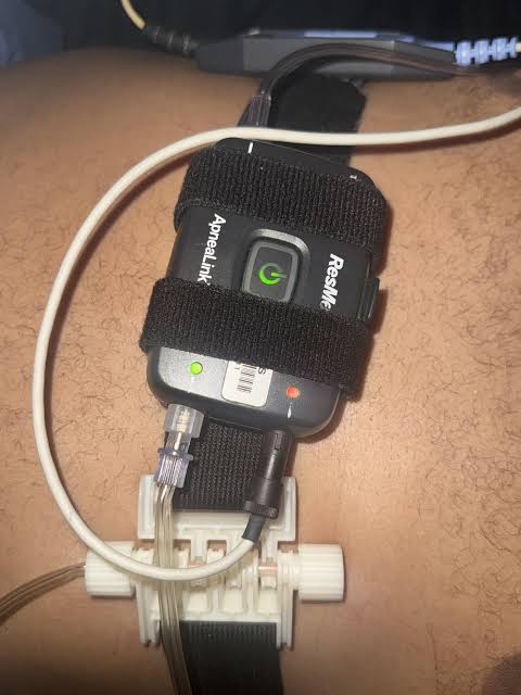 Dispositivo sujeto al pecho con el cinturón, con el botón central iluminado en verde y una luz de accesorio verde y otra roja debajo